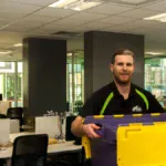 Kiwi Movers staff member carrying storage crate during office move in London